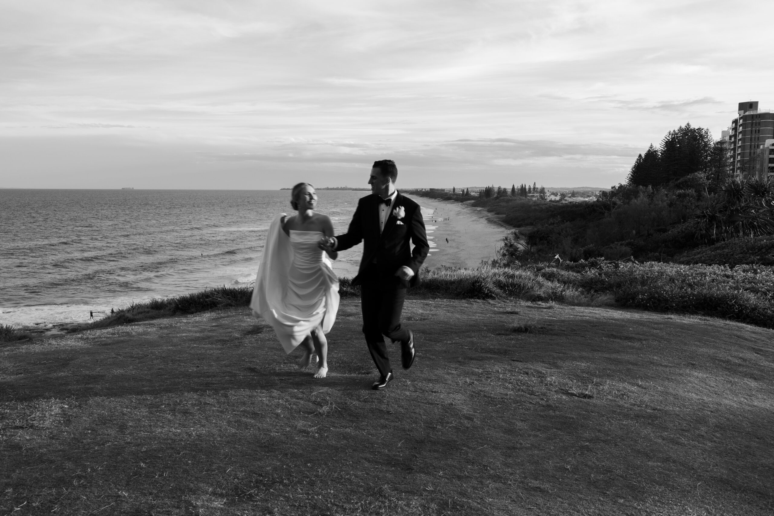 Newlyweds walking together from pandanus shade towards the Sunshine Coast shoreline